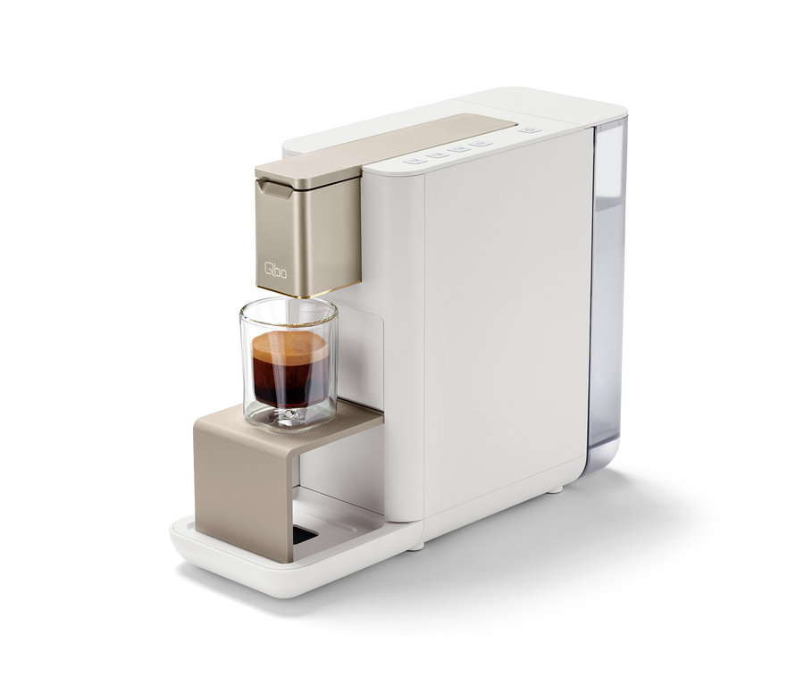 Qbo ICONIC Light Gold Kaffeemaschine mit einer Tasse Espresso.