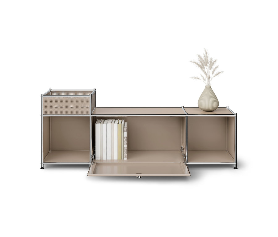 Ein hellbeiges modulares Aufbewahrungsmöbel mit Chromrahmen. Der linke Bereich hat ein offenes Fach und einen erhöhten, perforierten Korb. Der mittlere Bereich hat ein offenes Fach mit Büchern und eine offene Klapptür. Der rechte Bereich hat ein offenes Fach, darauf steht eine gerippte Vase mit getrockneten Federpflanzen.