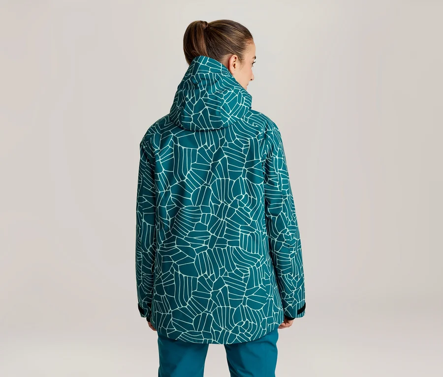 Frau von hinten, trägt eine türkise Jacke mit weißem geometrischem Muster und türkise Hose. Ihr Haar ist hochgesteckt, der Kopf leicht nach rechts gedreht.