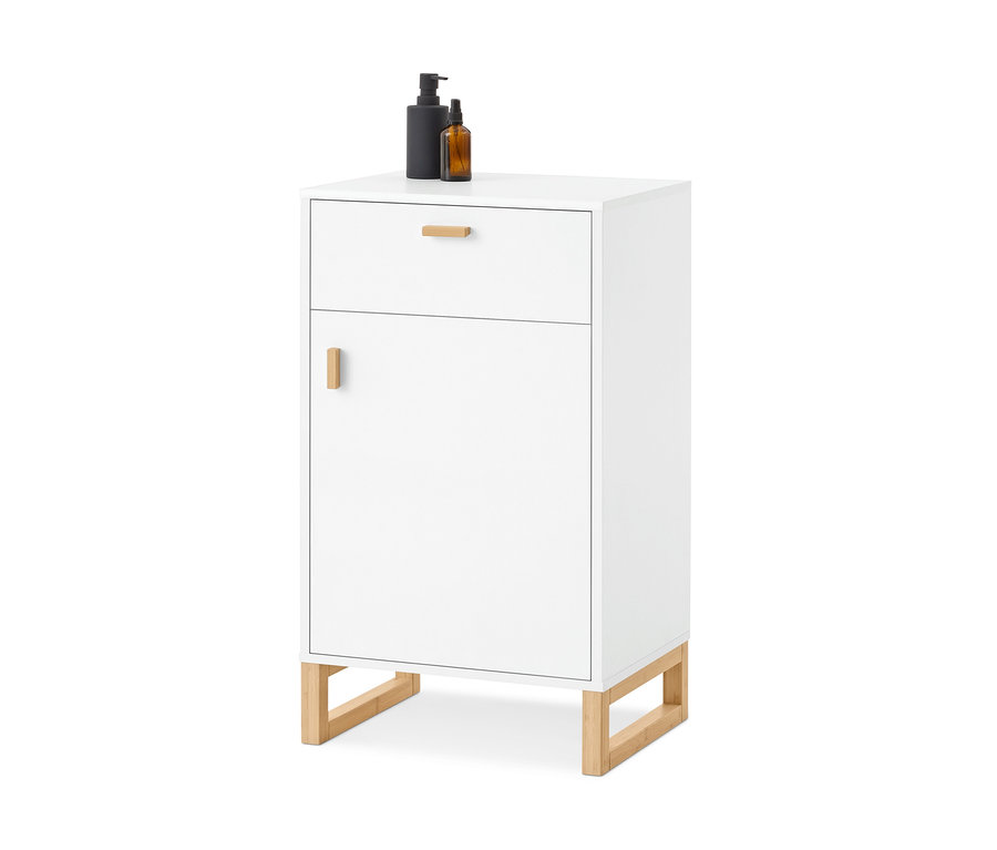 Weißer Schrank mit einer Schublade und einer Tür, beide mit Holzgriffen, auf Holzbeinen. Oben stehen eine schwarze Pumpspenderflasche und eine bernsteinfarbene Sprühflasche.