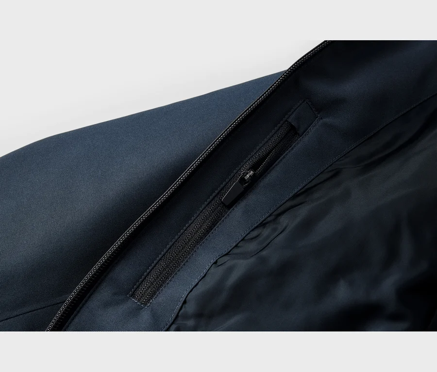 Nahaufnahme einer dunkelblauen Jacke mit einem Hauptreißverschluss und einem teilweise geöffneten Taschenreißverschluss an der inneren Patte, der ein dunkelblaues Futter zeigt.