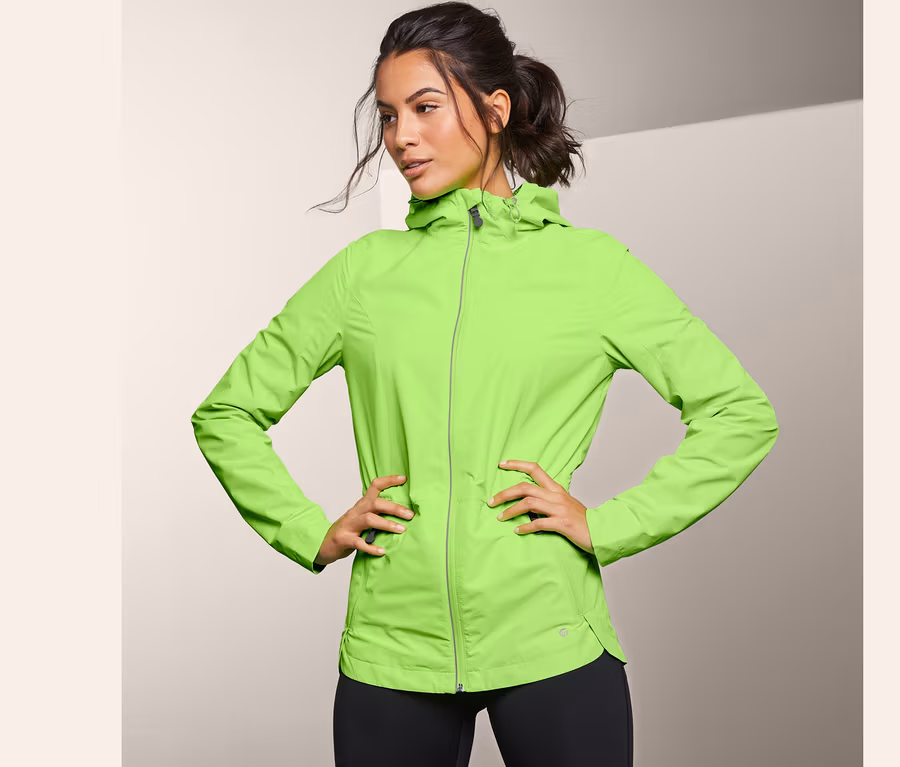 Frau posiert in neongrüner Windprotection-Laufjacke.