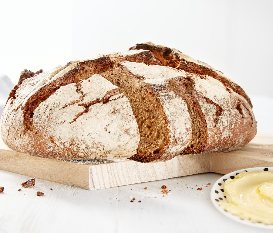 Ein Laib Brot auf einem Holzbrett neben einem Teller Butter.