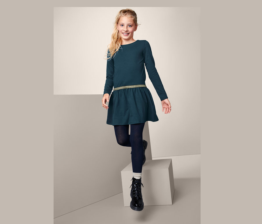 Mädchen steht auf einem weißen Würfel und trägt ein marineblaues Jerseykleid.
