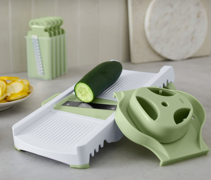 Gurke liegt auf Multireibe. Daneben liegen geschnittene Gurken und Zucchini.