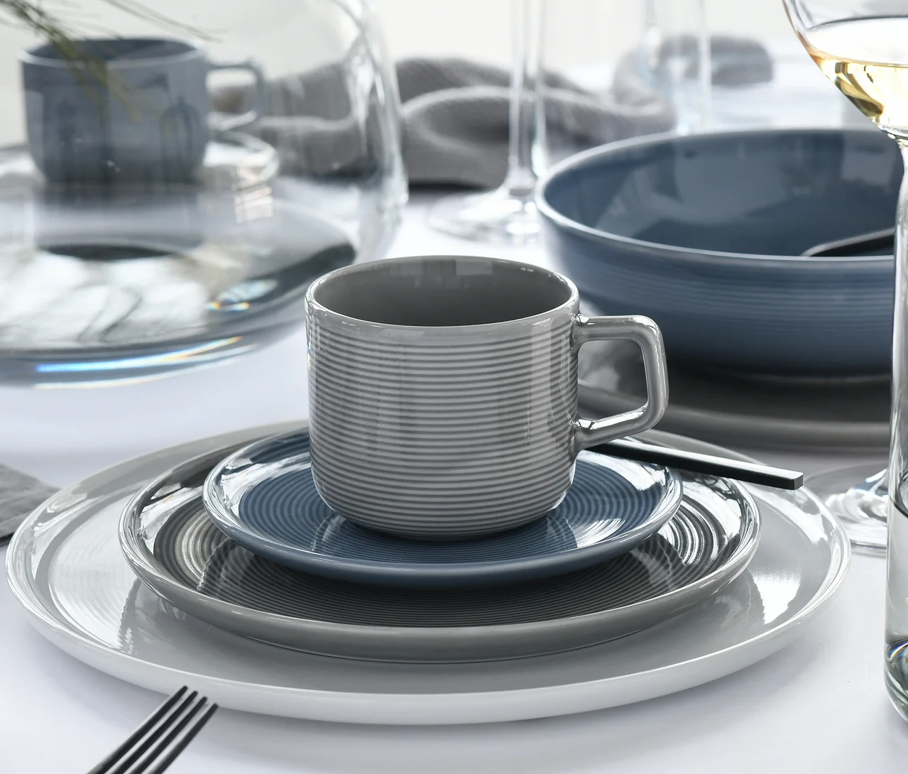 Gedeckter Tisch mit creaTable Service »Session Urban«: gestreifte graue Tasse auf blauer Untertasse, grauer und weißer Teller, blauer Schale.