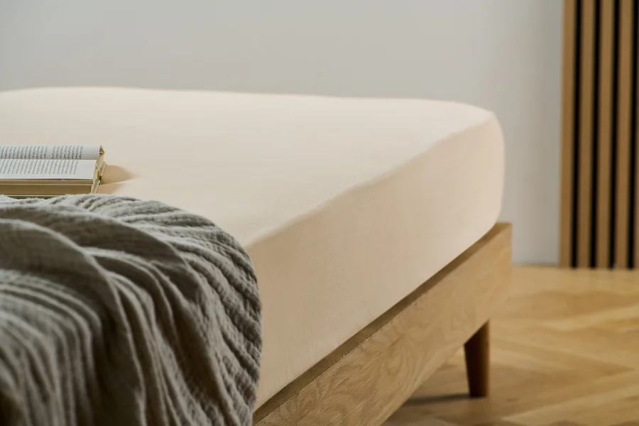 Ein cremefarbenes Biber-Spannbettlaken auf einem Bett mit einem Buch und einer grauen Decke.
