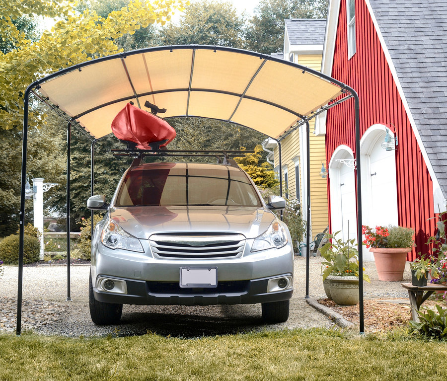 Ein silbernes Auto mit einem roten Kajak auf dem Dach parkt unter einem Runddach-Carport.