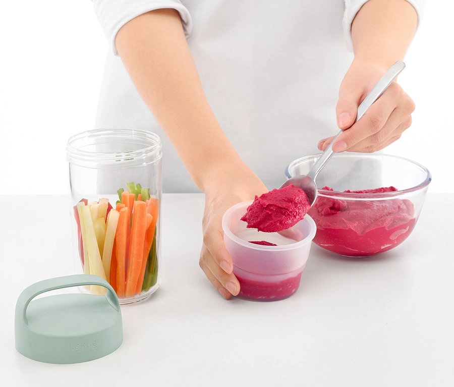 Frau löffelt Rote Bete aus einer Schüssel in eine To-go-Lunchbox. Daneben steht ein Glas mit Gemüse und ein Deckel.