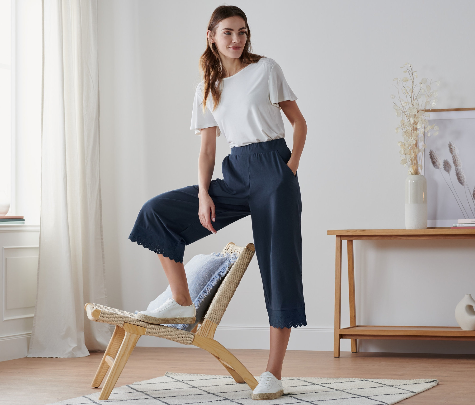 Eine Frau posiert mit einem Bein auf einem Stuhl, sie trägt eine Culotte mit Stickerei.