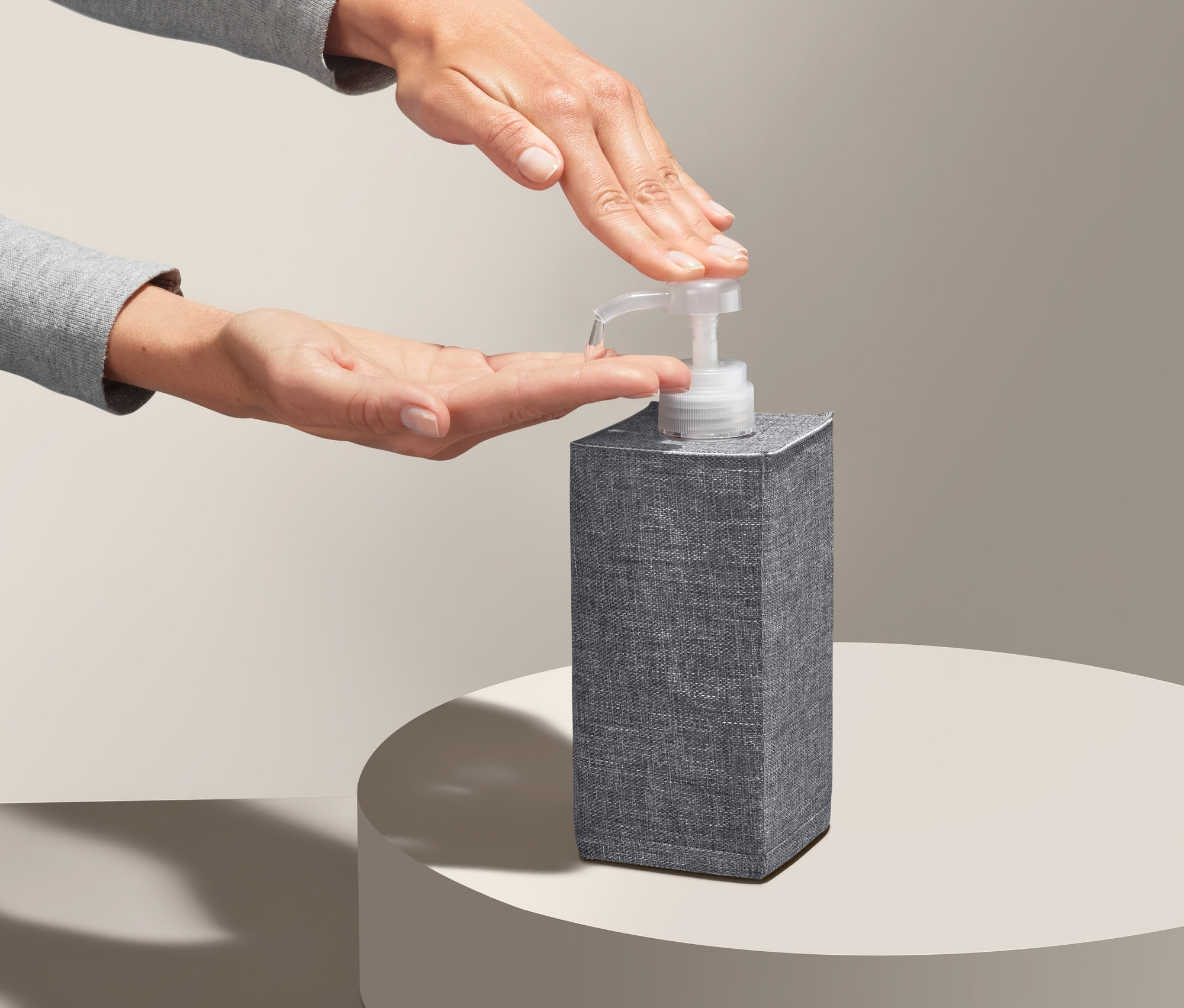 Eine Person benutzt eine graue Desinfektionsmittelbox mit Spender auf einem runden Sockel.