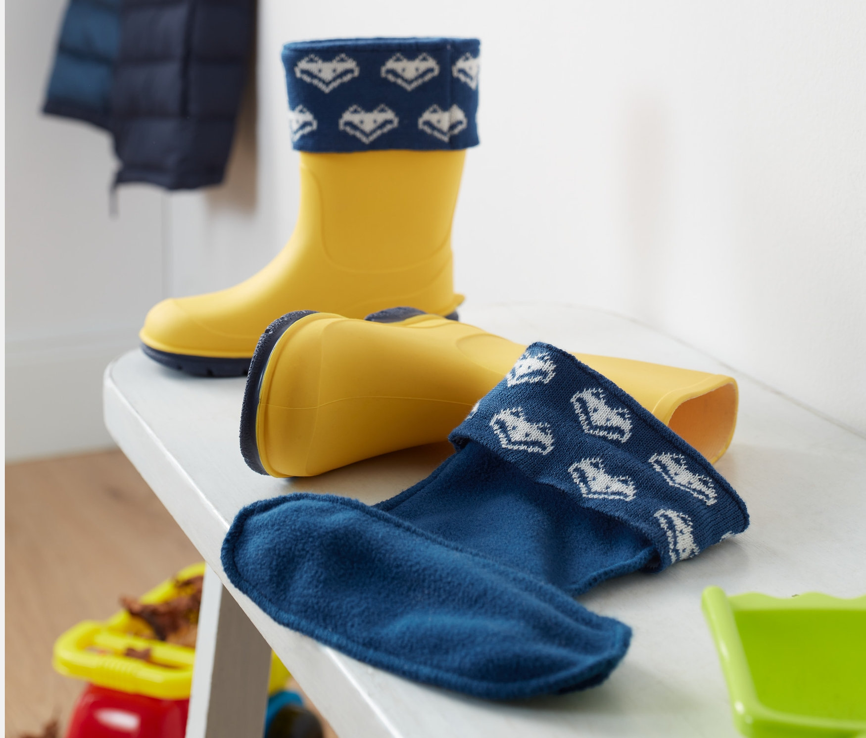 Gelbe Gummistiefel mit Regenstiefel-Stulpe auf einer weißen Bank.