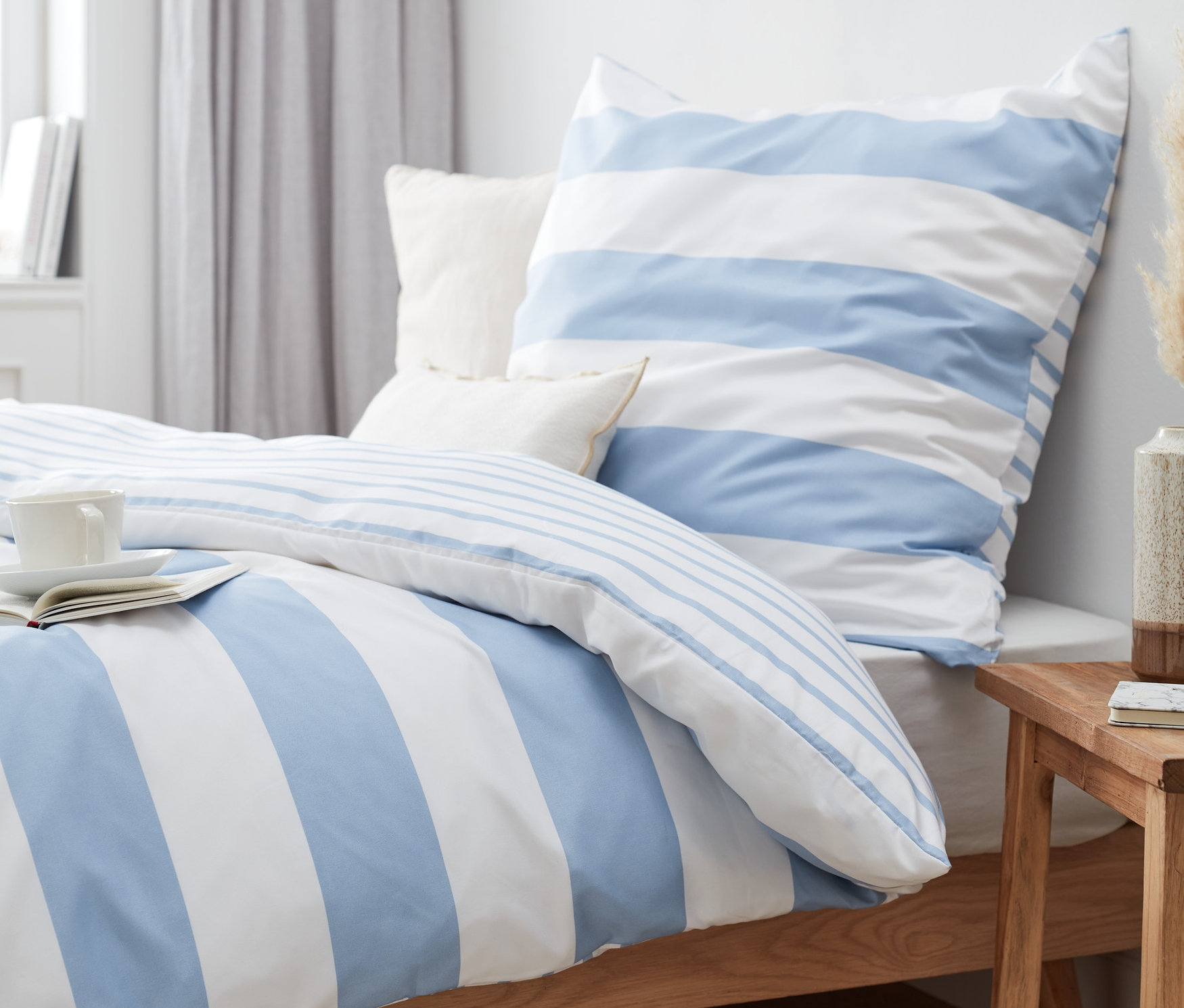 Blau gestreifte Microfaser-Bettwäsche (Normalgröße und Übergröße) auf einem Bett mit Buch und Tasse.