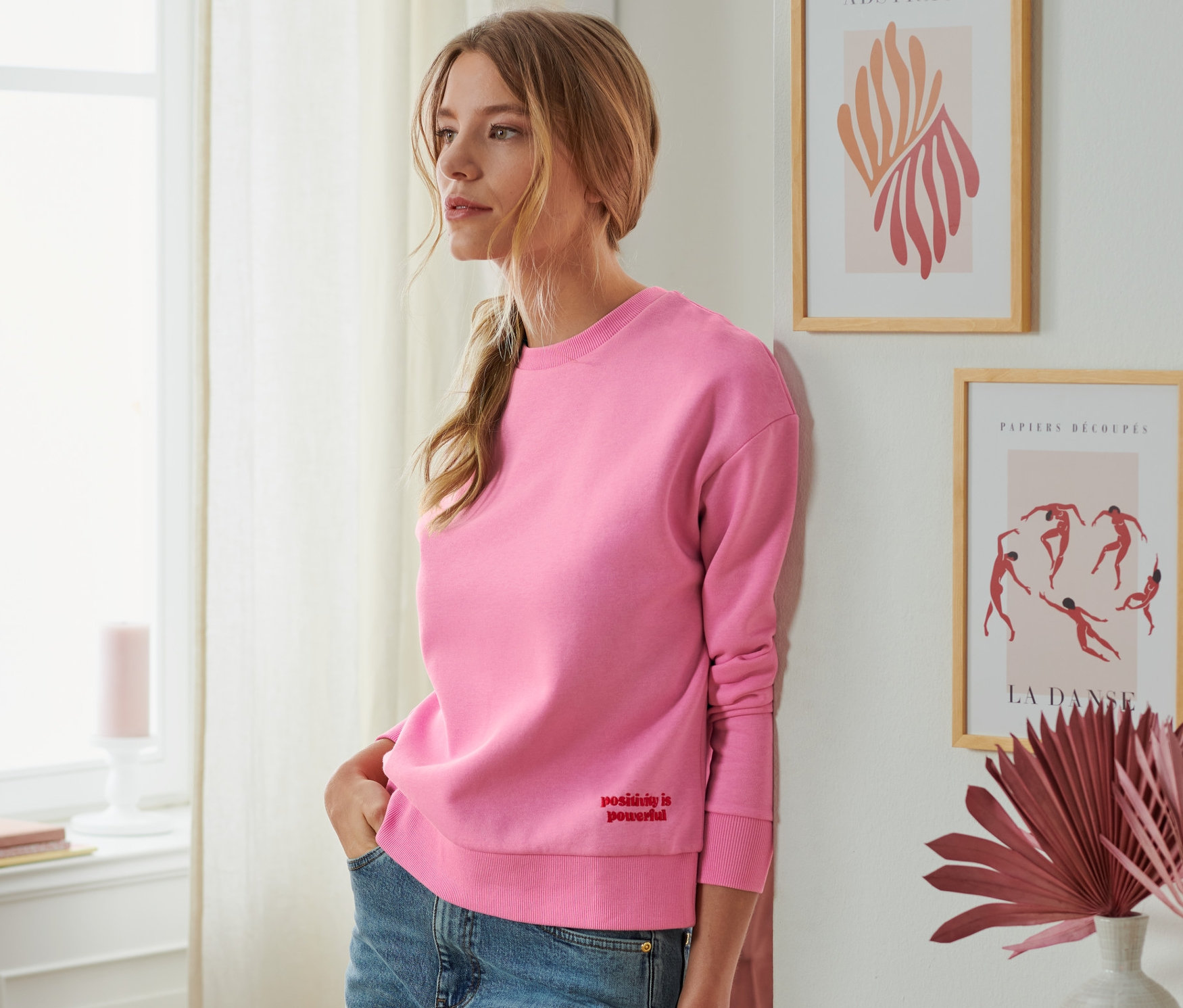 Eine Frau lehnt an der Wand und trägt ein Sweatshirt.