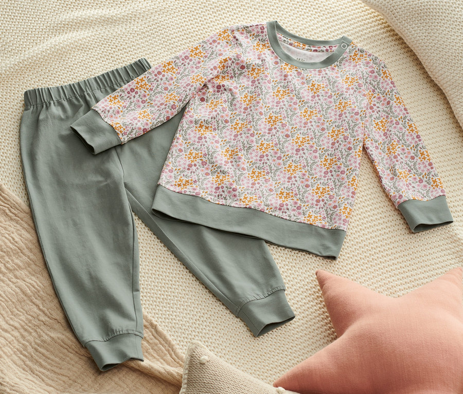 Auf einer cremefarbenen Strickdecke liegen ein grüner Pyjama und zwei Kissen.