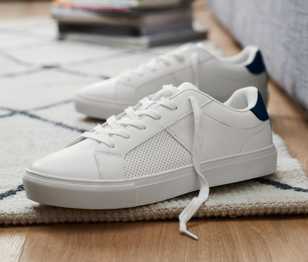 Zwei Sneaker stehen auf dem Boden neben einem grauen Sofa.