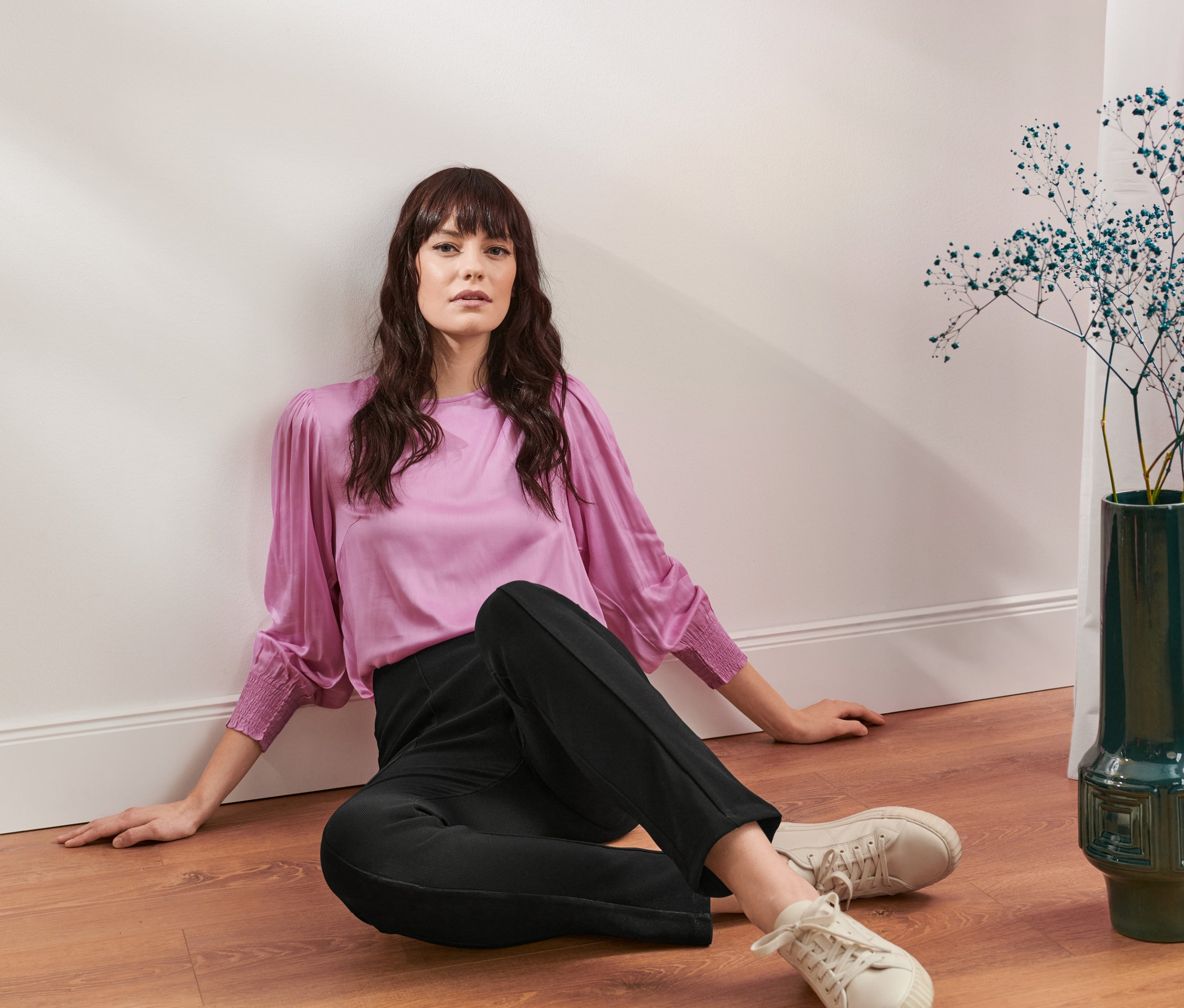 Frau sitzt auf dem Boden und trägt eine Bluse.