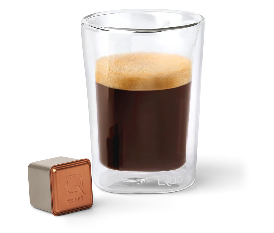 Eine Qbo Caffè BUNA ENTETA Kapsel neben einem Glas Kaffee.