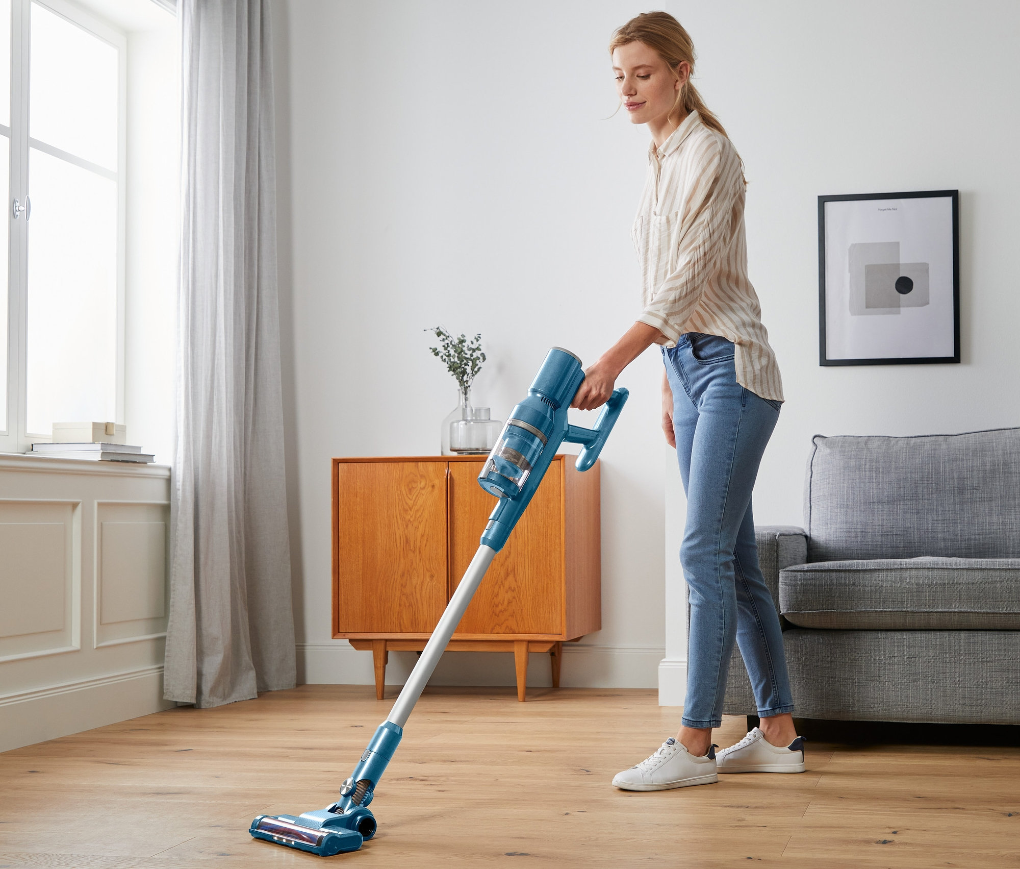 Frau saugt den Boden mit einem blauen digitalen Akkusauger.