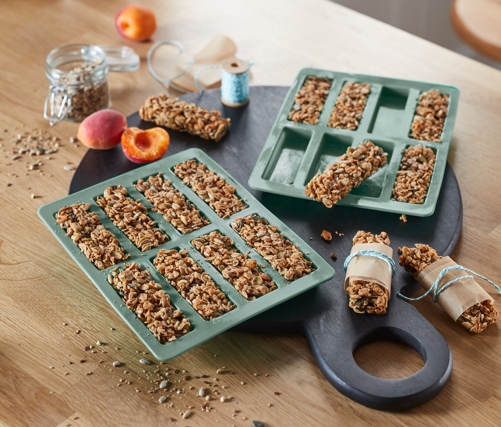 Zwei grüne 2 Müsliriegel-Backformen liegen nebeneinander auf einem Tisch. In einer Form sind fünf Riegel, in der anderen acht.