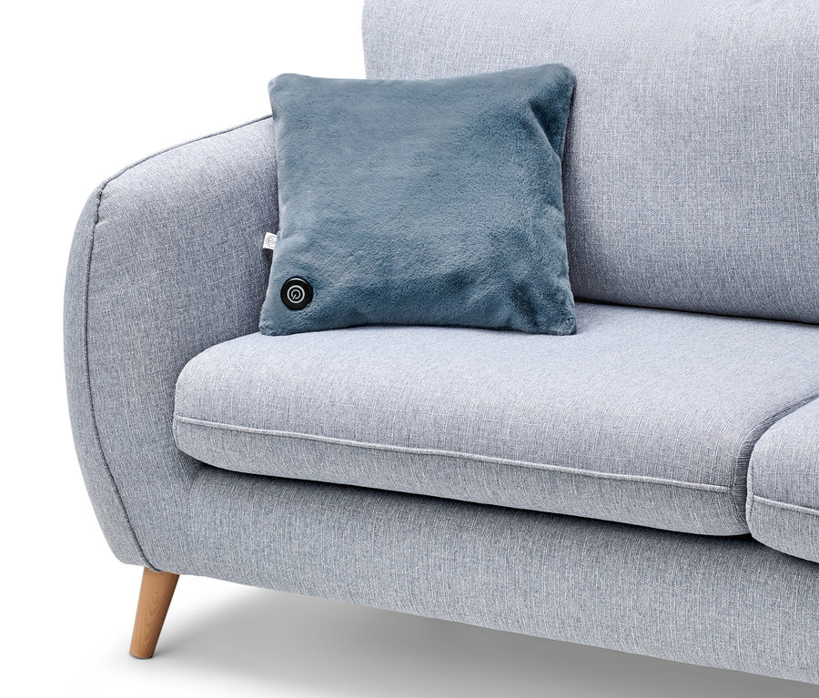 Ein blaues Akku-Heizkissen liegt auf einem grauen Sofa.