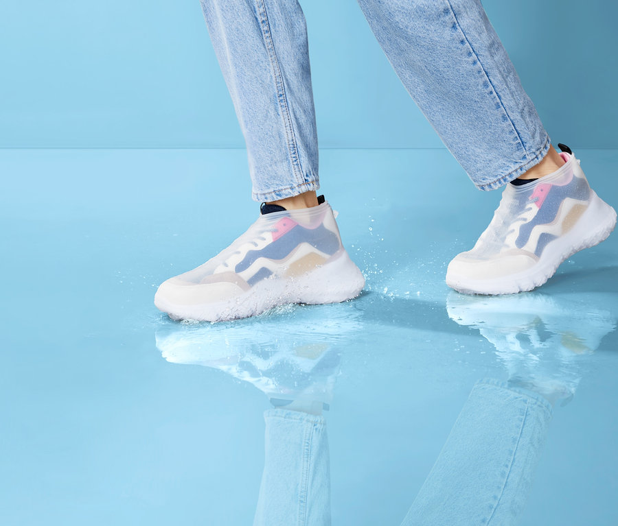 Beine in Jeanshosen gehen in Regen-Überziehschuhen auf nassem Untergrund.