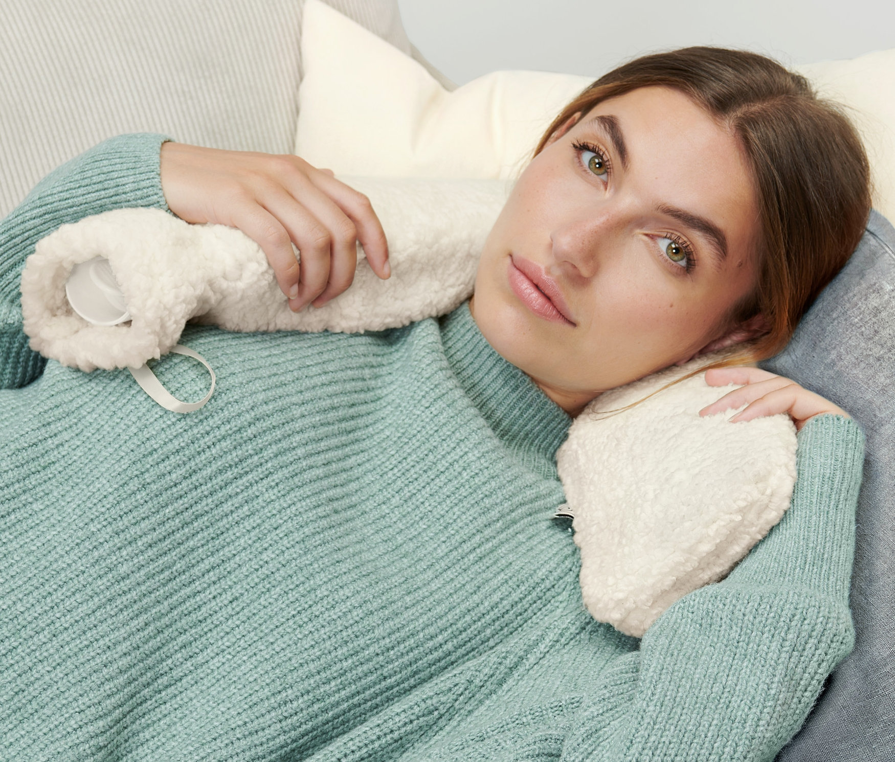 Frau liegt mit Schlauch-Wärmflasche auf Sofa.