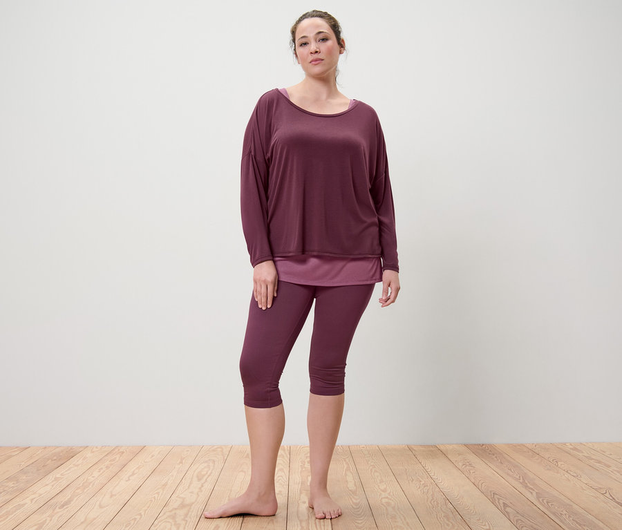 Frau steht barfuß und trägt ein 2-in-1-Sportshirt und eine 3/4-Sporttight in Pflaume.