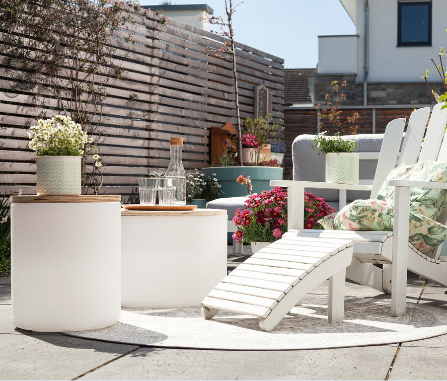 Eine Außenterrasse mit weißen Möbeln und Blumen in Töpfen. Eine 8 seasons design LED-Leuchte ist auch vorhanden.