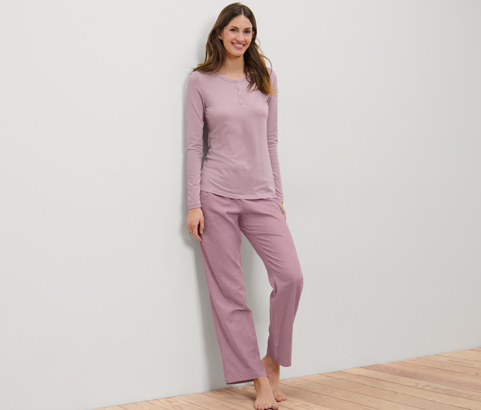 Frau lehnt an Wand und trägt Flanell-Pyjama.