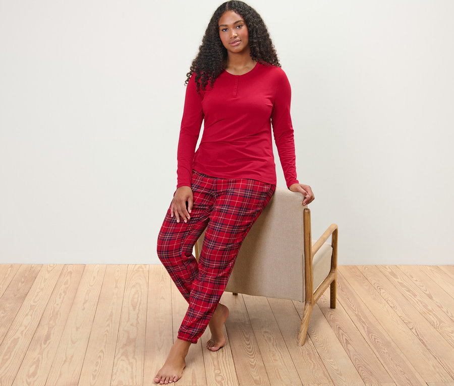 Eine Frau posiert, an einen Stuhl gelehnt, und trägt einen karierten Flanellpyjama.