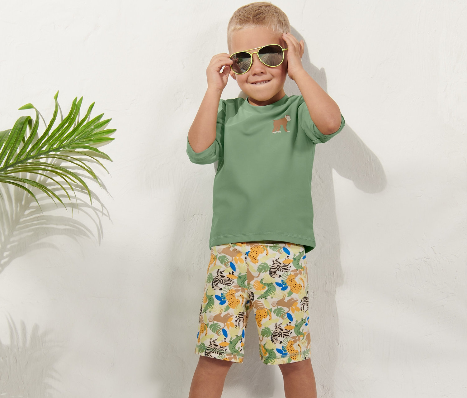 Junge setzt Sonnenbrille auf, trägt Kleinkind-Kombi mit UV-Schutz 80.