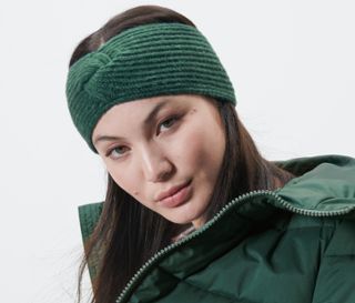Frau trägt ein dunkelgrünes Strick-Stirnband und eine grüne Jacke.