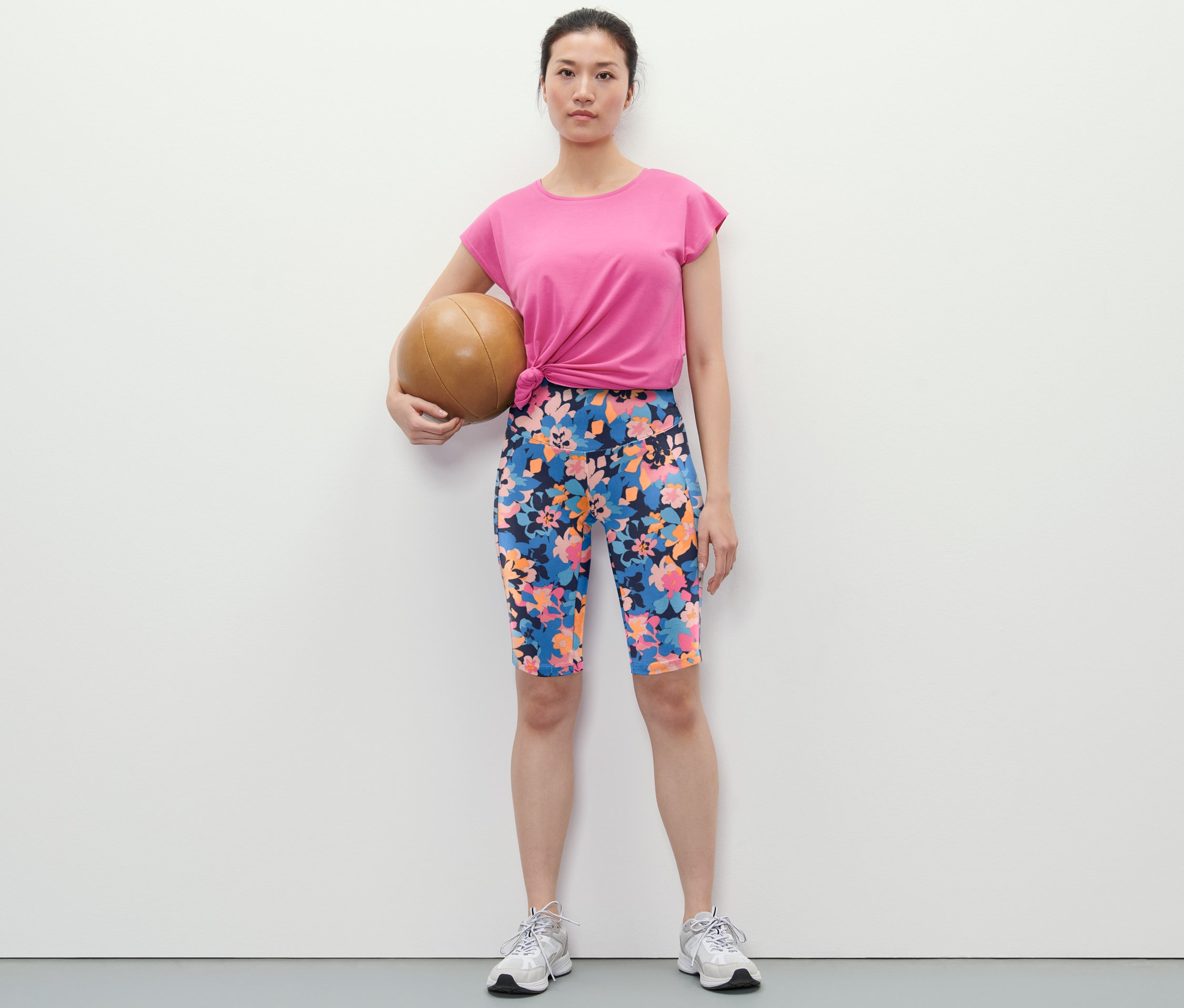 Frau hält Medizinball und trägt Sportradler mit Alloverprint, T-Shirt und Turnschuhe.