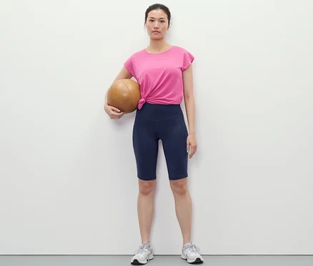 Frau hält einen Basketball und trägt dunkelblaue Sportradler.