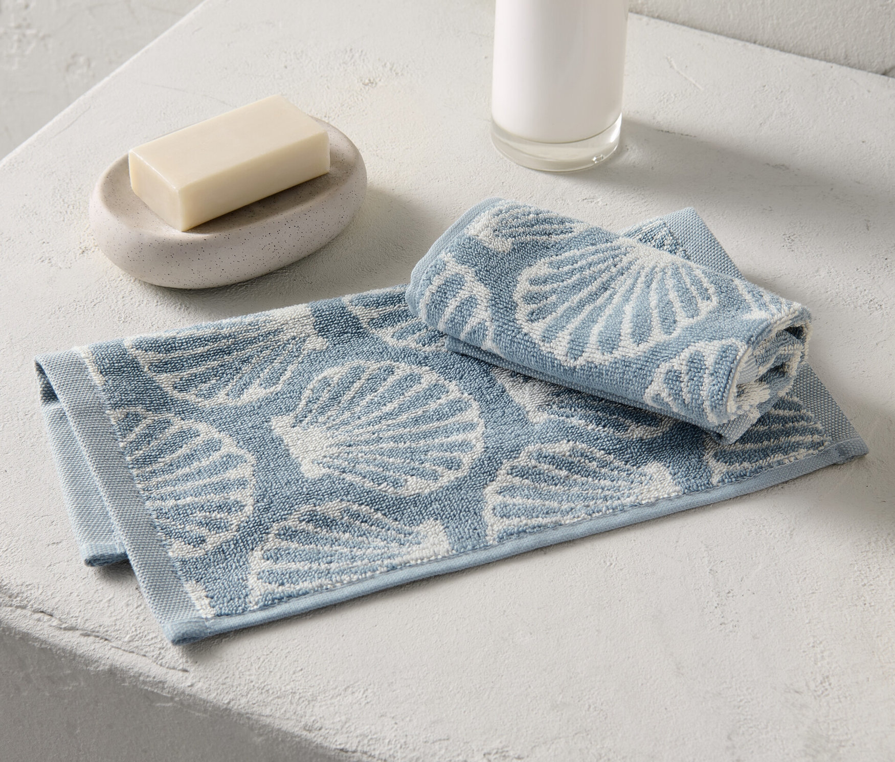 Zwei Seiftücher mit Muschelmuster liegen neben Seife und Seifenspender.