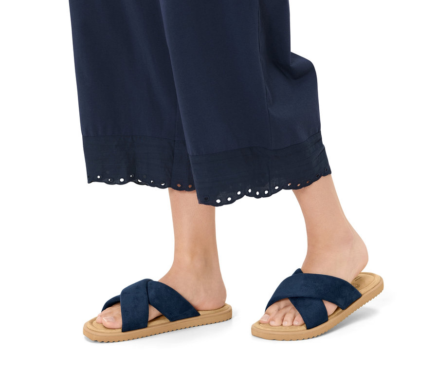 Beine einer Frau in marineblauer Hose und Komfortsandalen.