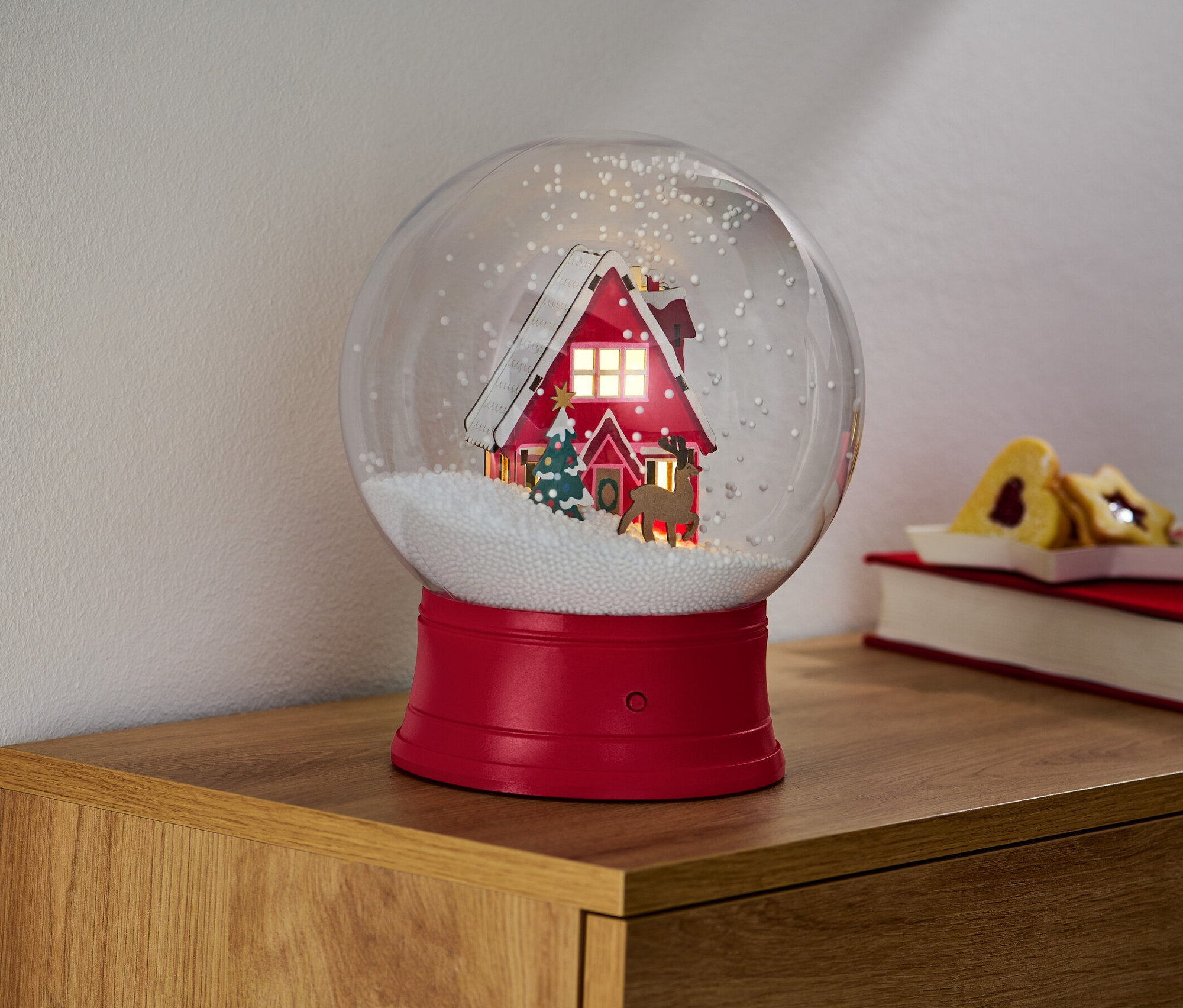 Eine große LED-Schneekugel mit einem Haus, Bäumen und einem Rentier.
