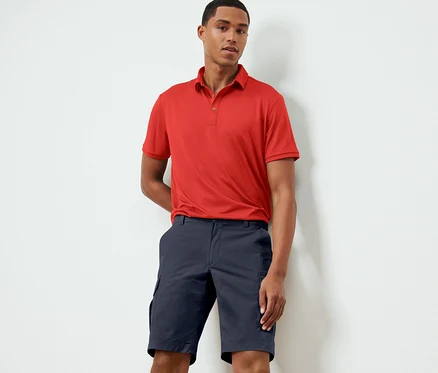 Mann posiert in rotem Polohemd und blauen Funktionsshorts.