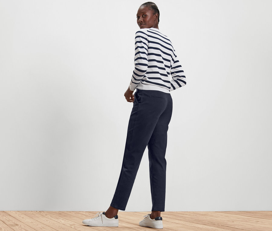 Frau posiert in dunkelblauen Chinos und einem gestreiften Pullover.
