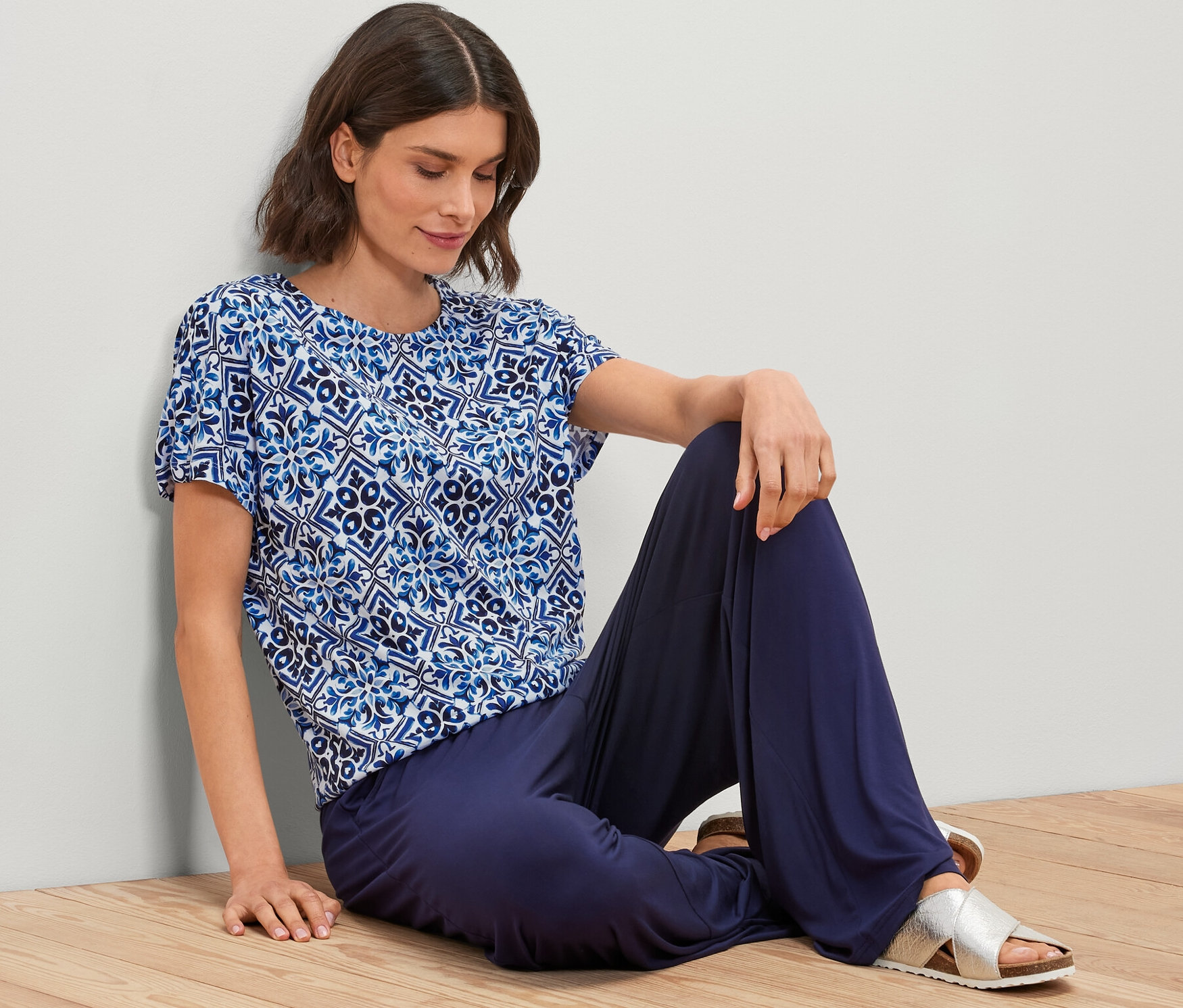 Frau sitzt am Boden und trägt ein blaues, bedrucktes Blusenshirt.