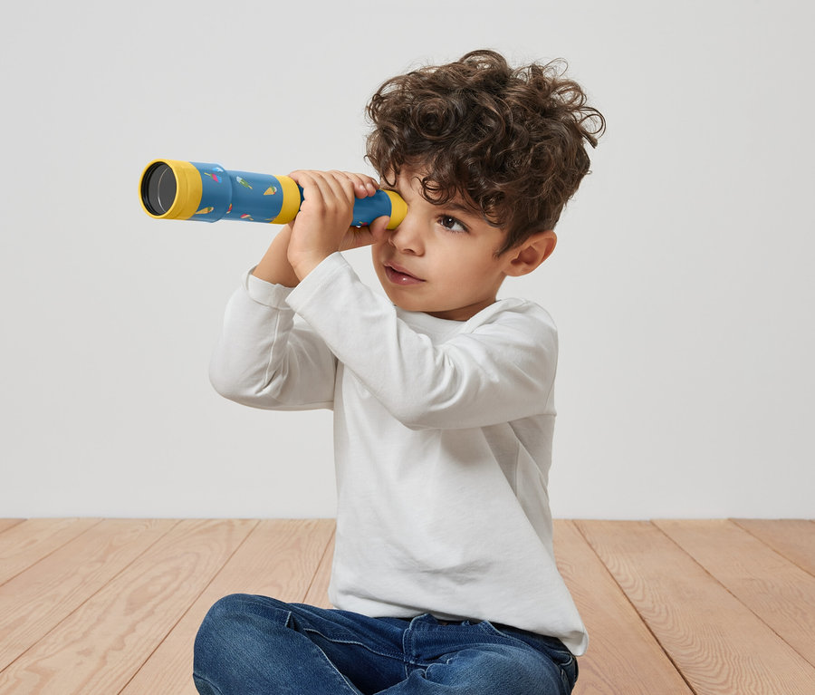 Junge sitzt am Boden und schaut durch ein Spiel-Fernrohr.