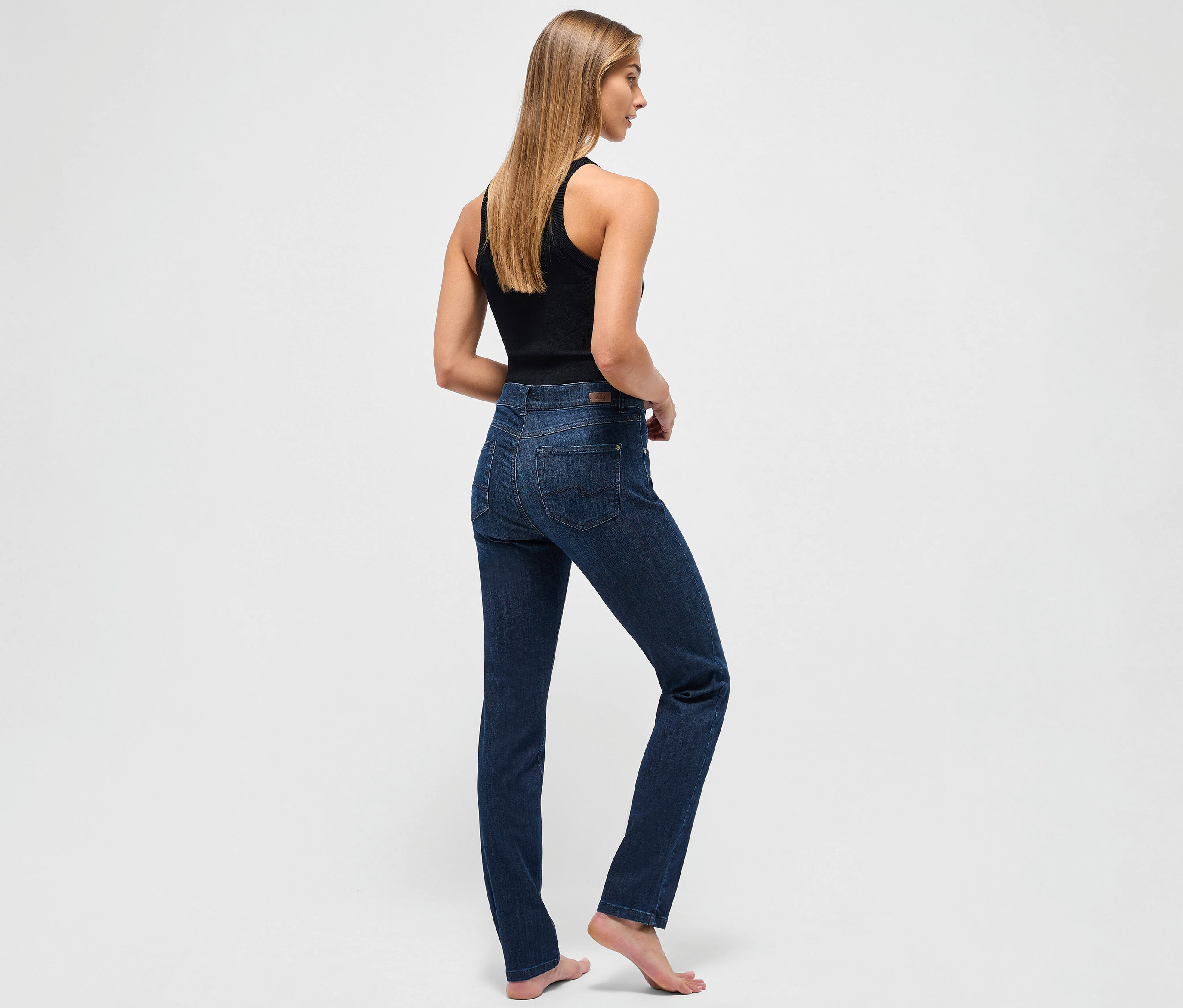 Eine Frau steht mit dem Rücken zum Betrachter und trägt eine dunkelblaue Angels Jeans »Cici« Slim Fit und ein schwarzes Tanktop.