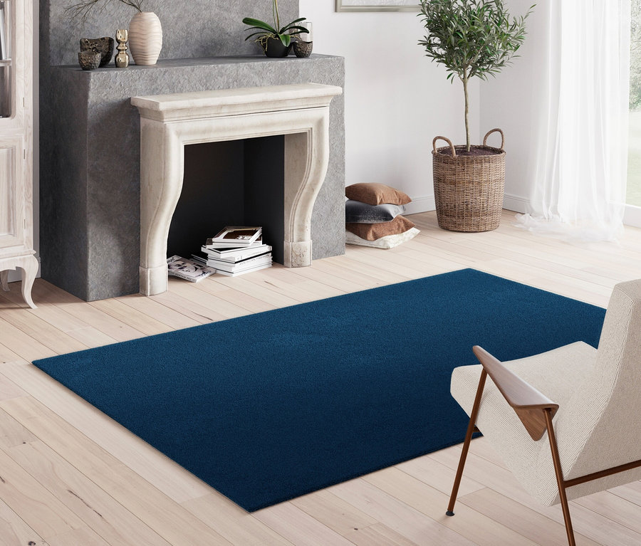 Blauer Teppich »Mellow« liegt in einem Wohnzimmer mit Kamin und Sessel.