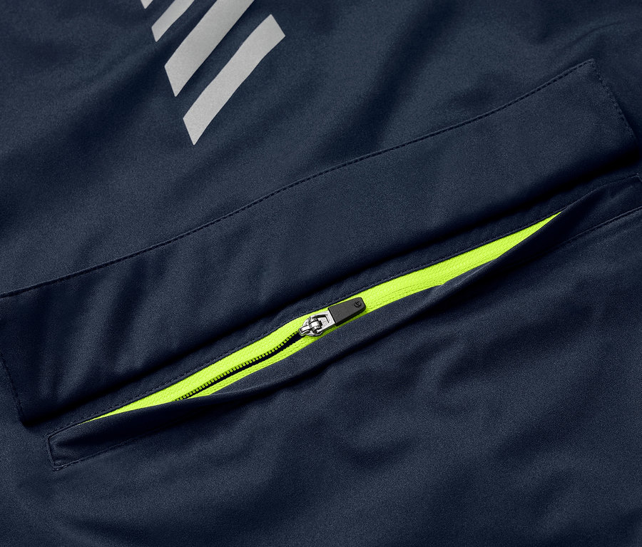 Detail einer blauen Rad-Regenjacke mit neongrünem Reißverschluss an der Tasche und reflektierenden Elementen.