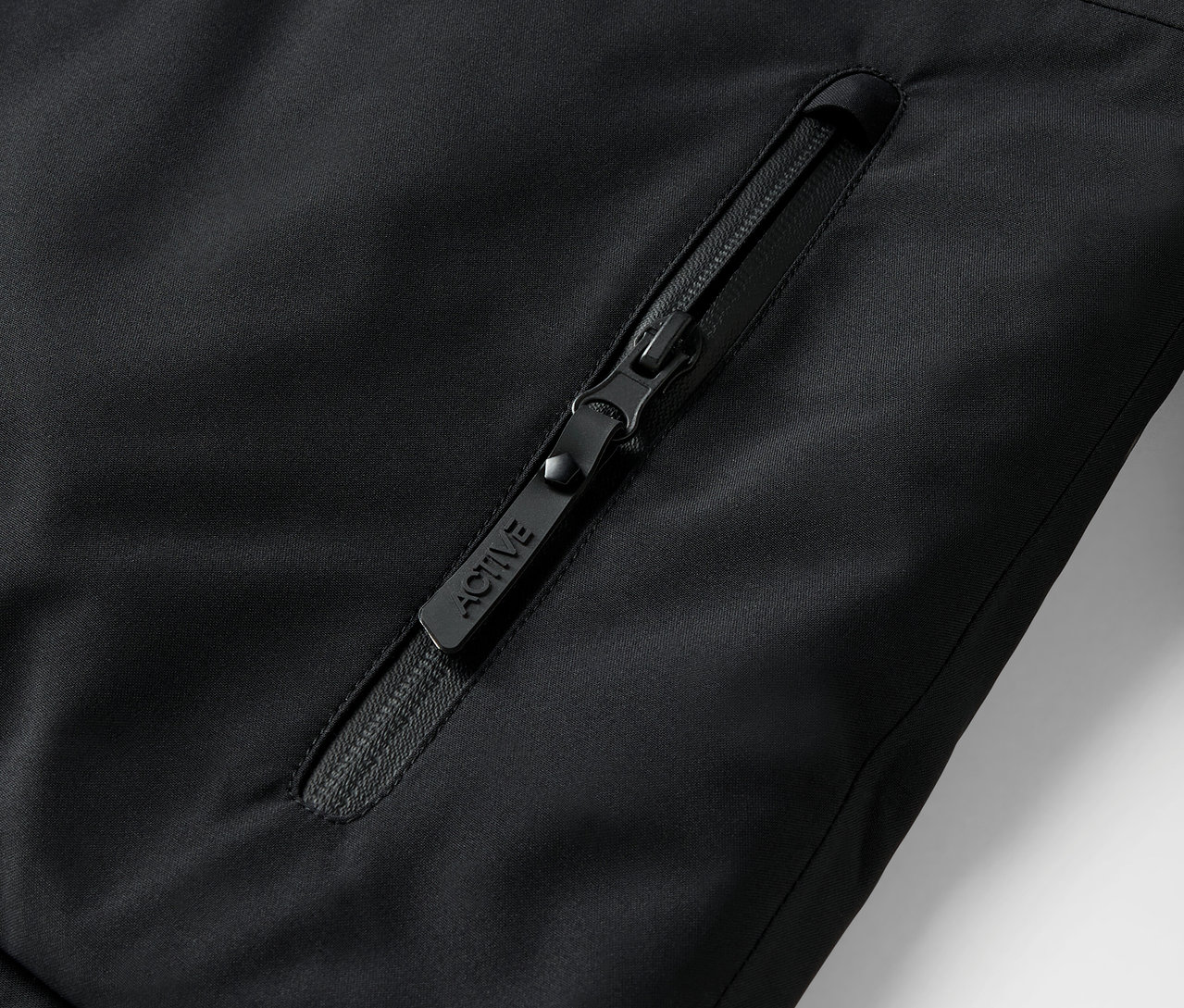 Detailaufnahme eines schwarzen Reißverschlusses an einer Jacke mit der Aufschrift ACTIVE.