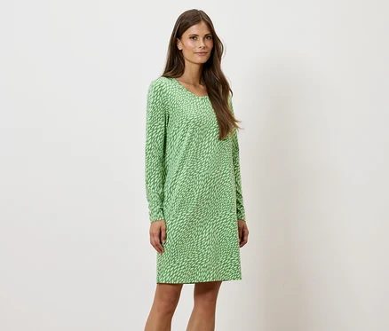 Eine Frau steht und posiert in einem grün gemusterten, langärmeligen Kleid.