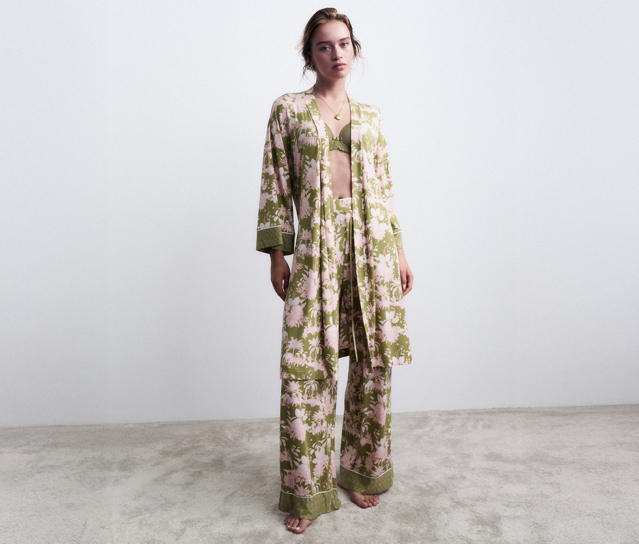 Frau steht barfuß in einem grünen, blumenverzierten Pyjama mit passendem Morgenmantel.