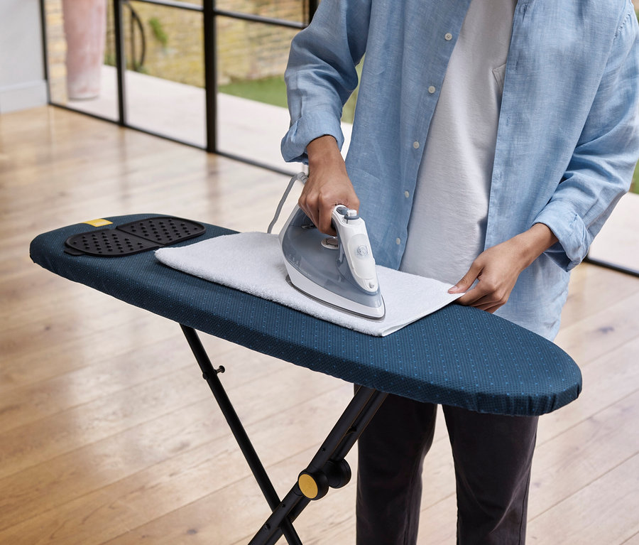 Person bügelt ein weißes Tuch auf einem blauen Bügelbrett.
