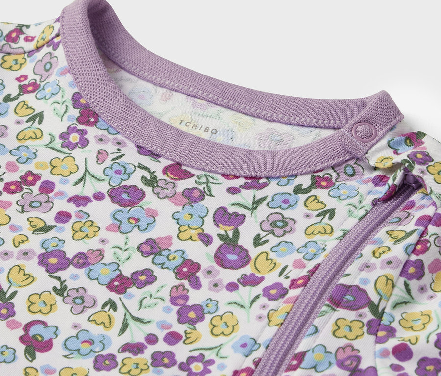 Detailansicht eines weißen Babykleidungsstücks mit lila und gelben Blumen und lila Saum.
